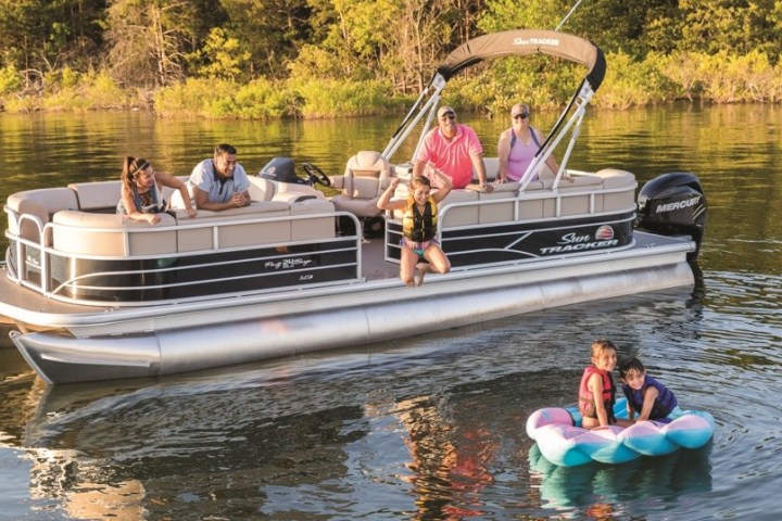 Group on pontoon boat with two children in life jackets on a float in the water.